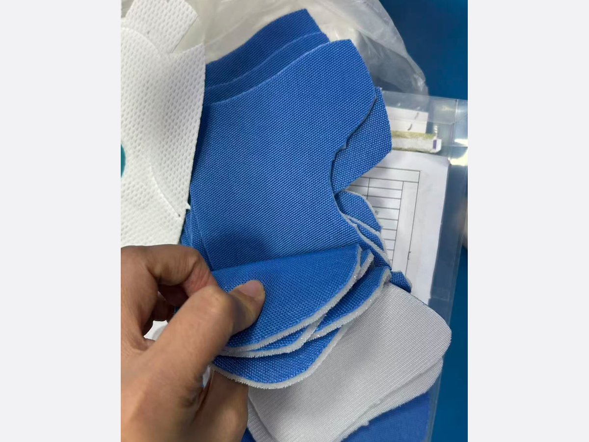 Cut blue mesh panels and white lining pieces for a shoe upper, held in one hand
