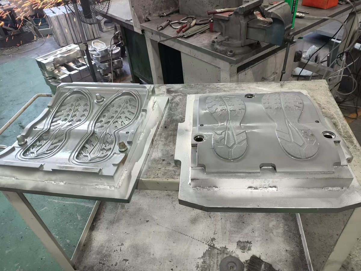Upper and lower halves of a metal sole mould on a bench in the tooling workshop, with a vice and hand tools behind