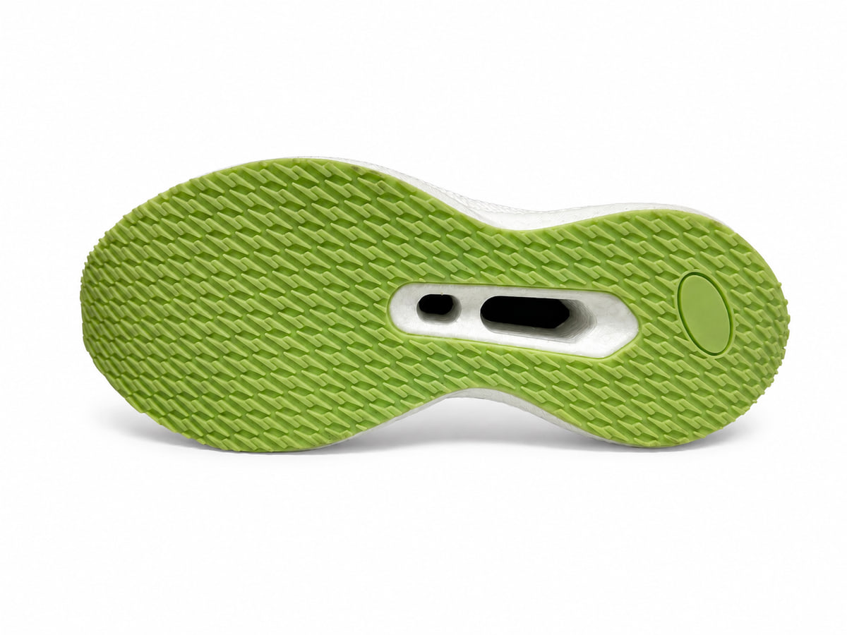 Underside of the same green sole, with a fine chevron tread and a white midfoot plate with cut-outs